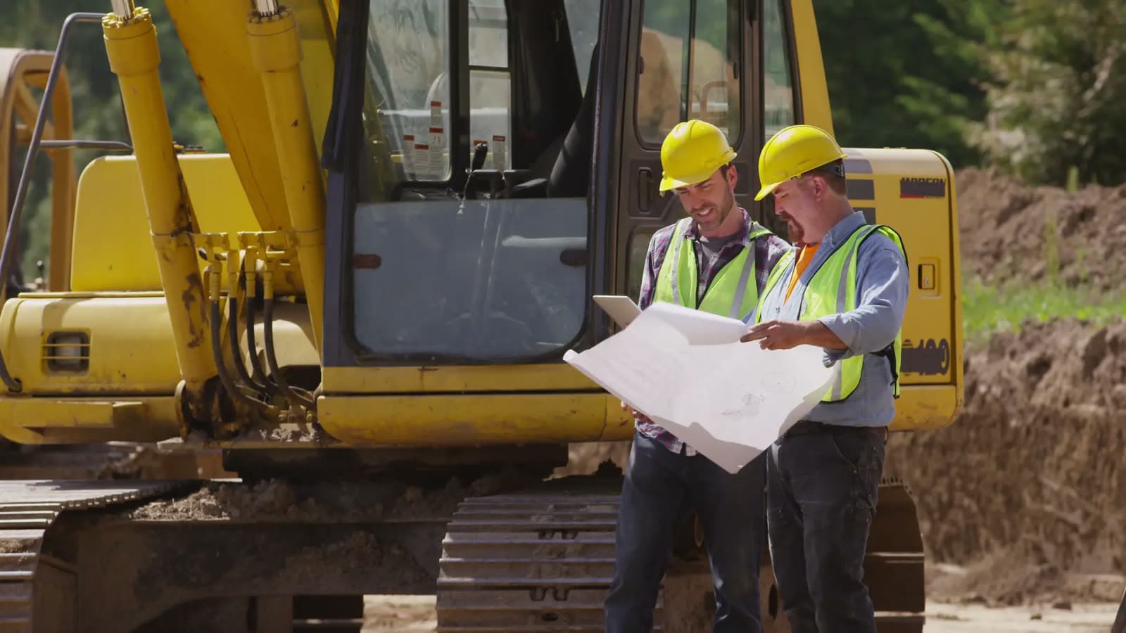 Two contractors reviewing plans in front of an excavator